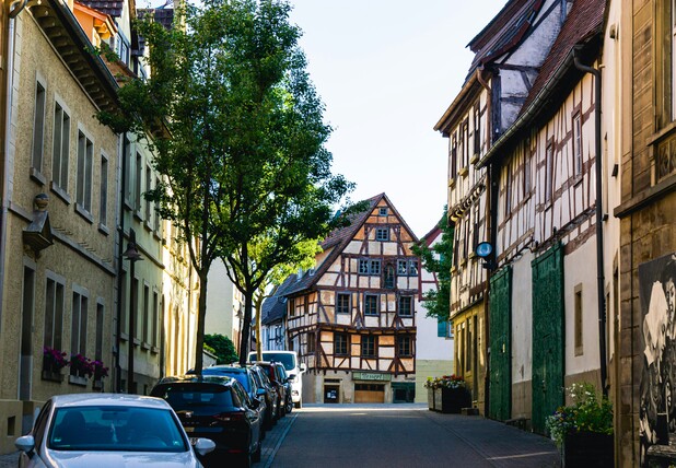 [Translate to English:] Straße in einer Kleinstadt mit historischen Fachwerkhäusern, Bäumen und parkenden Autos.