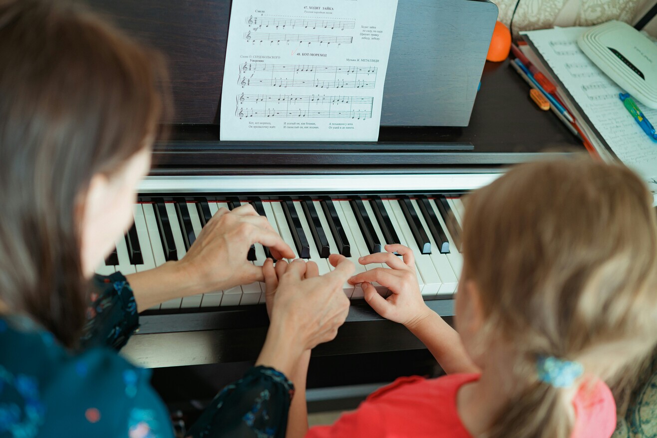 Eine Frau und ein Mädchen sitzen gemeinsam an einem Klavier und spielen Musik.
