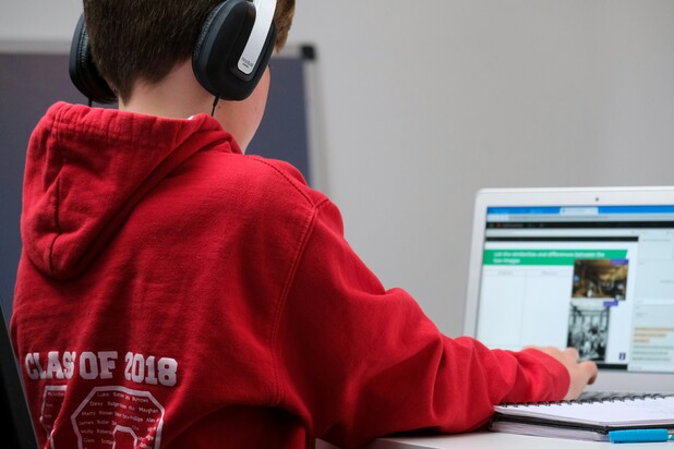 [Translate to English:] Ein Junge in rotem Kapuzenpullover sitzt mit Kopfhörern vor einem Laptop und nutzt diesen zum Lernen.