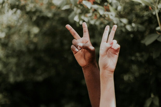 [Translate to English:] Eine Person hält eine Hand mit ausgestrecktem Zeige- und Mittelfinger als Friedenszeichen in die Luft. Im Hintergrund liegt Schnee.