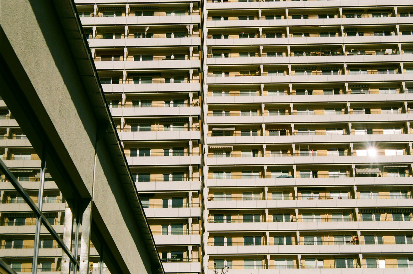 Mehrstöckiges Wohngebäude mit zahlreichen Balkonen und großen Fenstern in Berlin-Marzahn, aufgenommen aus der Froschperspektive vor klarem Himmel.