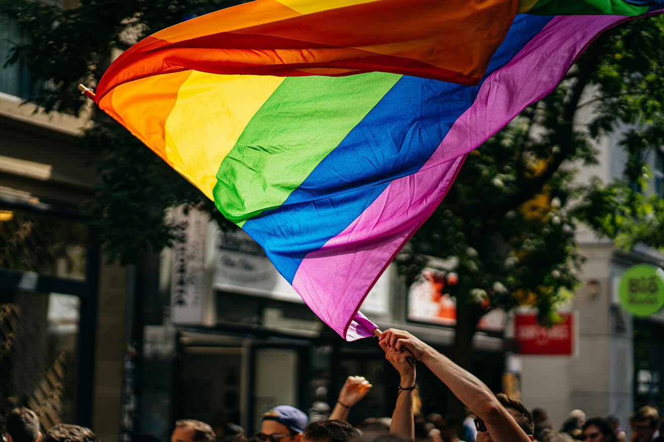 Menschen mit Regenbogenflaggen bei einer Pride-Demonstration im Freien.